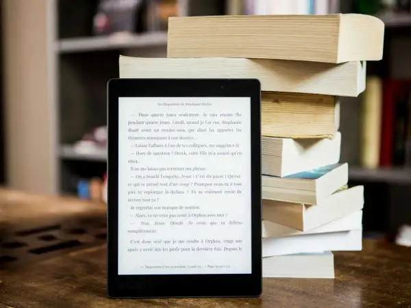 Liseuse affichant un roman, à côté d'une pile de livres. Idéal pour trouver un epub gratuit sans inscription et plonger dans une nouvelle histoire.
