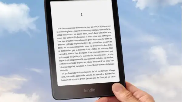 Main tenant un Kindle, un livre numérique de Nextory, sur fond de ciel bleu et nuageux.