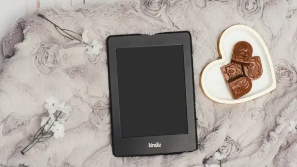 Un Kindle Vella posé sur une couverture douce, avec des chocolats en forme de cœur et des fleurs blanches.