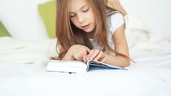 Une jeune fille de 11 ans, allongée sur un lit, est absorbée par la lecture d'un livre.
