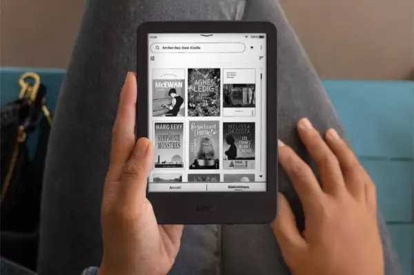 Une personne tient un Kindle affichant des livres, une invitation à découvrir un livre Kindle gratuit.