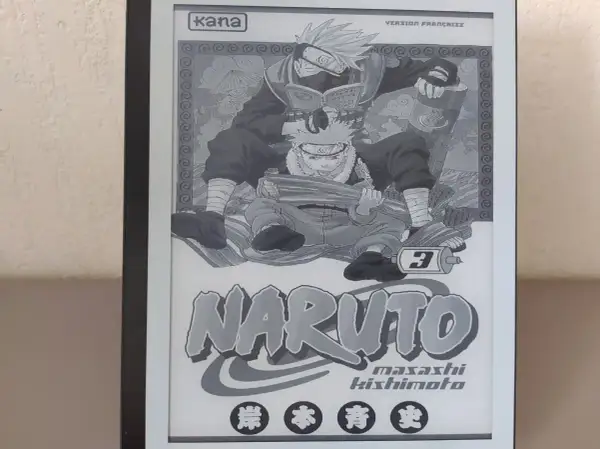 Un **manga sur liseuse** affiche la couverture du tome 3 de Naruto, avec Kakashi lisant par-dessus Naruto.