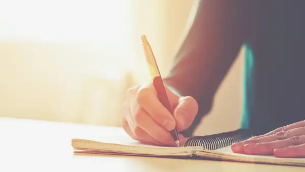 Main d'une personne écrivant dans un carnet. Une histoire vraie prend forme, un témoignage précieux consigné dans ce livre.