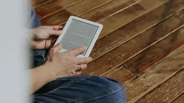 Une personne lit sur une tablette encre électronique, assise sur un plancher en bois.