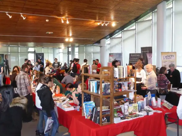 Foule dans un salon littéraire, admirant des livres et des affiches.